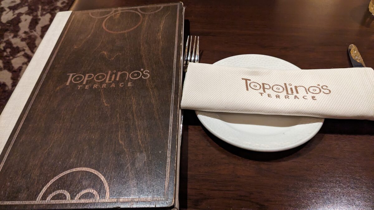 A picture of a menu, plate, and napkin from my family's dinner at Topolino's Terrace at Disney's Riviera Resort in Orlando, Florida